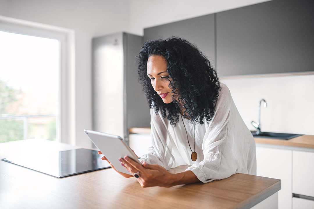 Woman in her kitchen leaning on a counter looking at a tablet