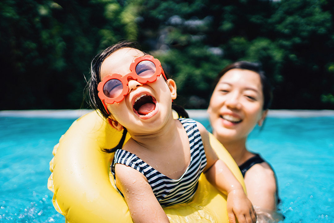 Smiling mother in a swimming pool with her daughter in a yellow floatie